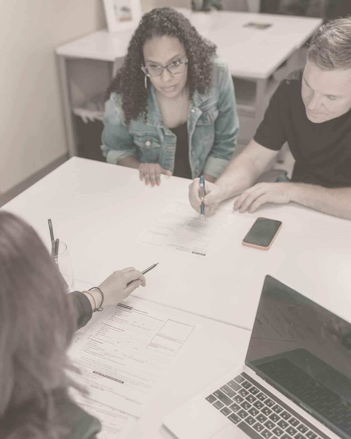 Three adults seated around a table reviewing printed paperwork together at a school meeting